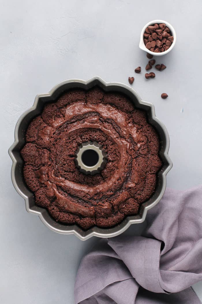 Baked chocolate bundt cake cooling in the pan on a gray counter