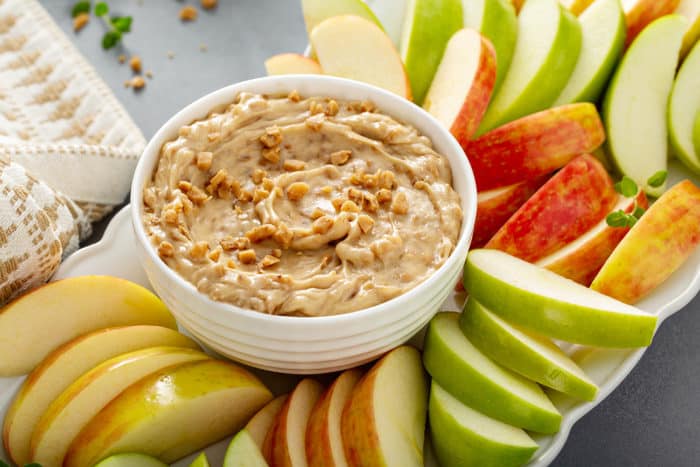 Bowl of toffee apple dip surrounded by slices of fresh red and green apples