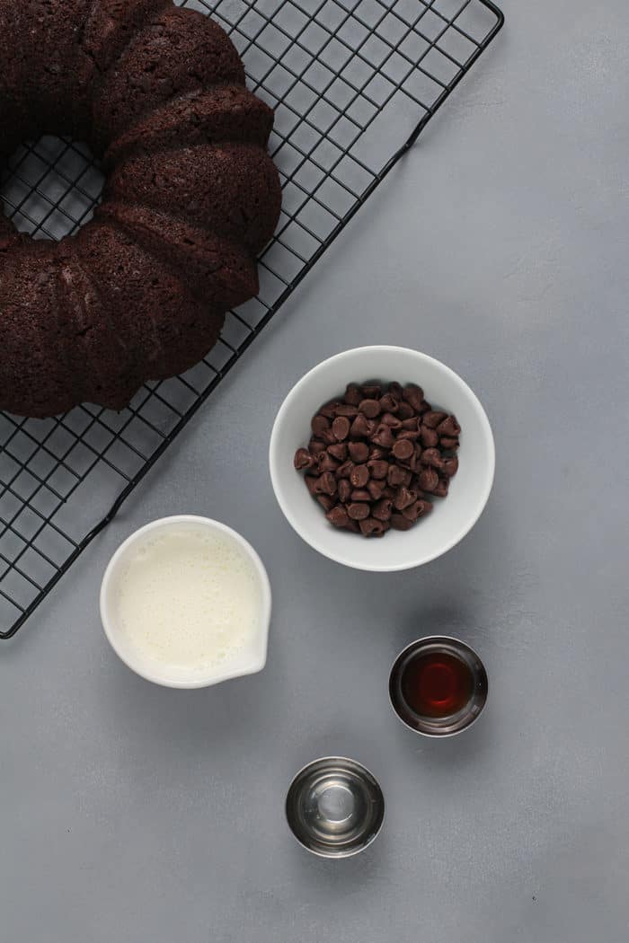 Ingredients for chocolate ganache next to a wire rack holding a chocolate bundt cake