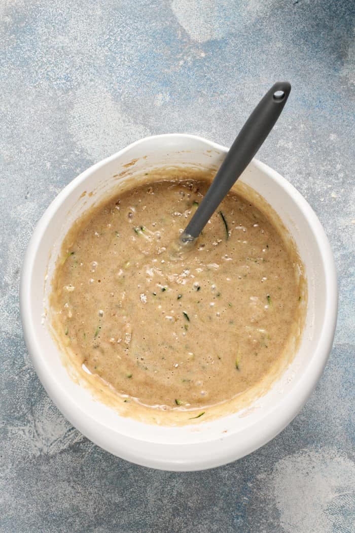 Spatula stirring together classic zucchini bread batter in a white bowl