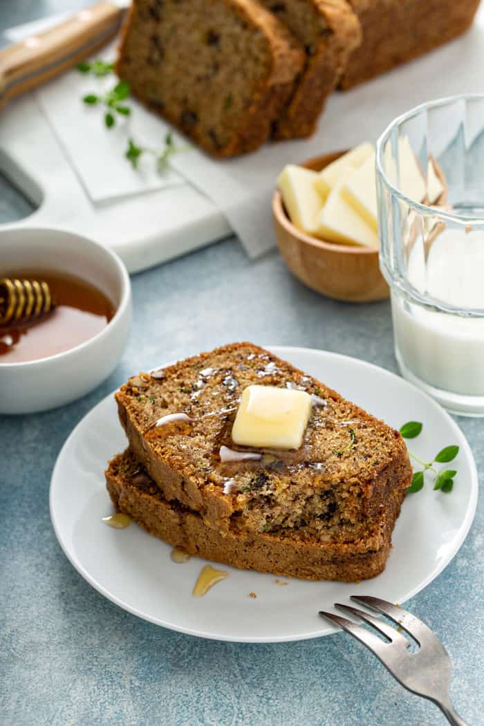 Two slices of classic zucchini bread on a plate, topped with butter and honey