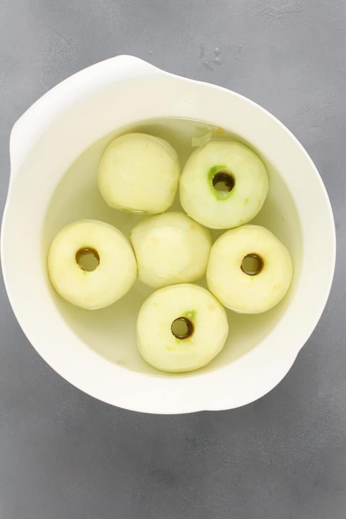 Peeled and cored apples set in a white bowl filled with water