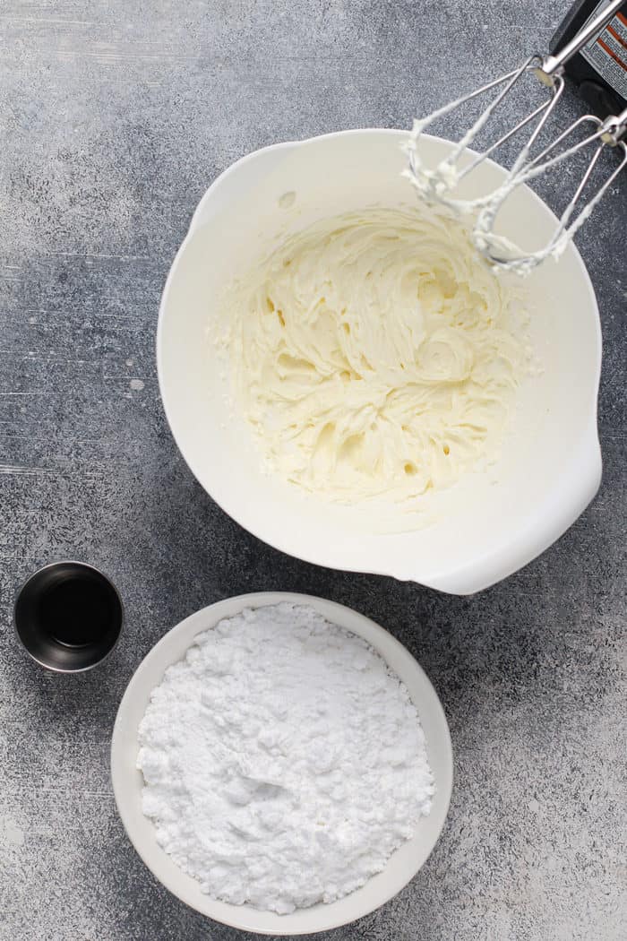 Cream cheese frosting being mixed together with a hand mixer in a white mixing bowl