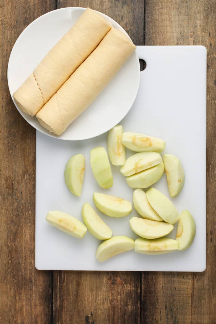 Sliced apples in a white cutting board next to crescent roll dough