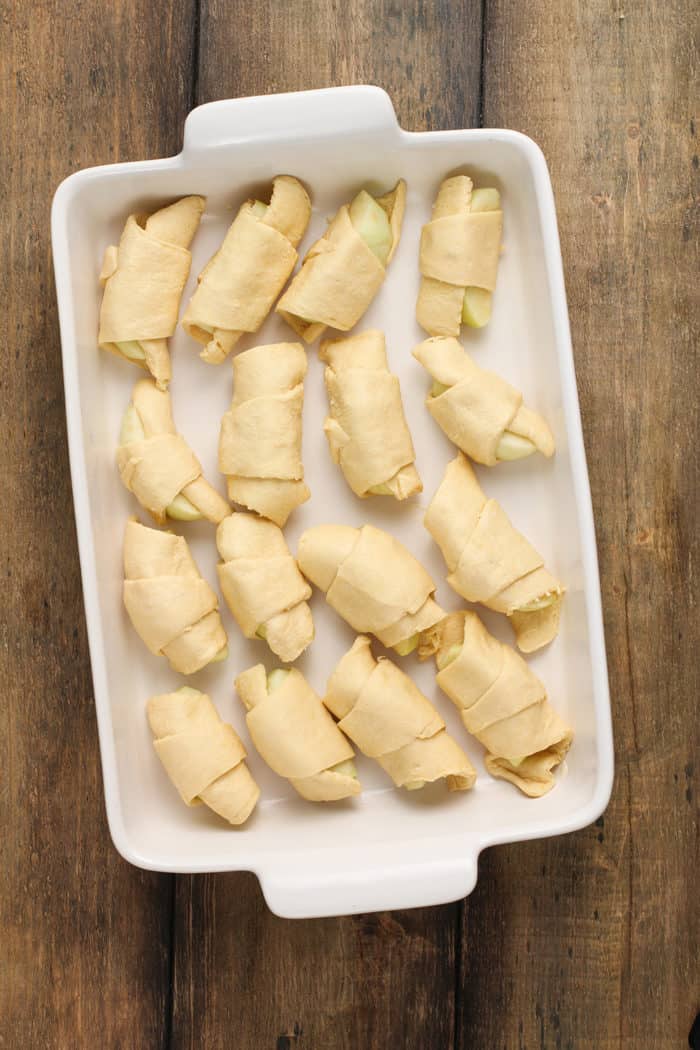 Apple slices wrapped in crescent roll dough arranged in a white baking dish