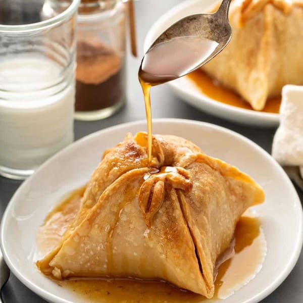 Spoon pouring sugar syrup over the top of a plated old-fashioned apple dumpling