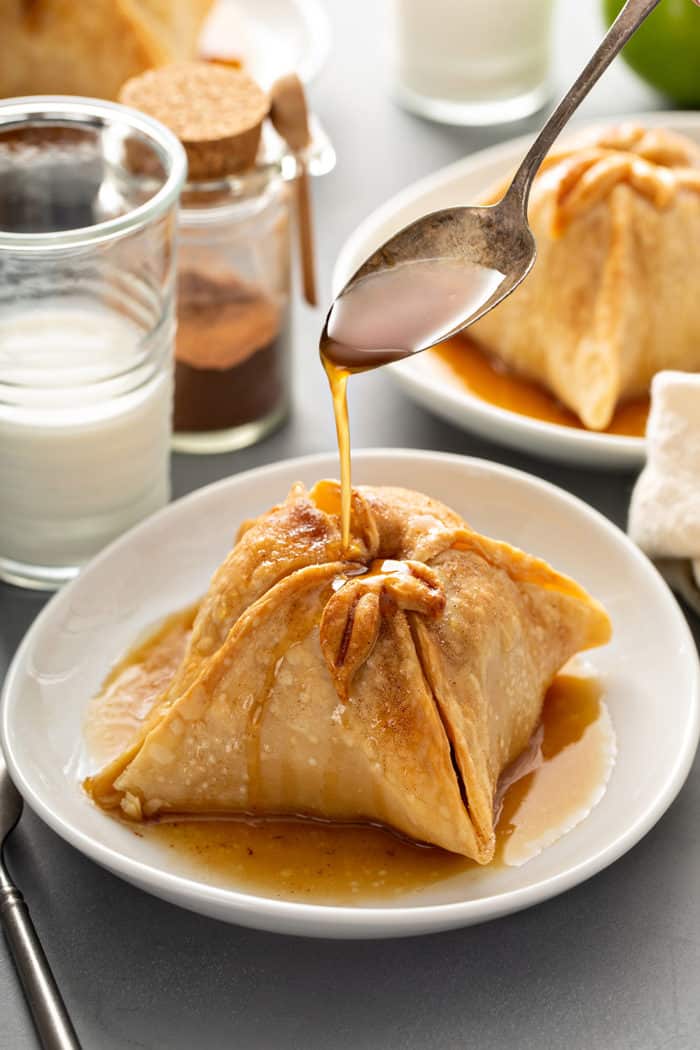 Spoon pouring sugar syrup over the top of a plated old-fashioned apple dumpling