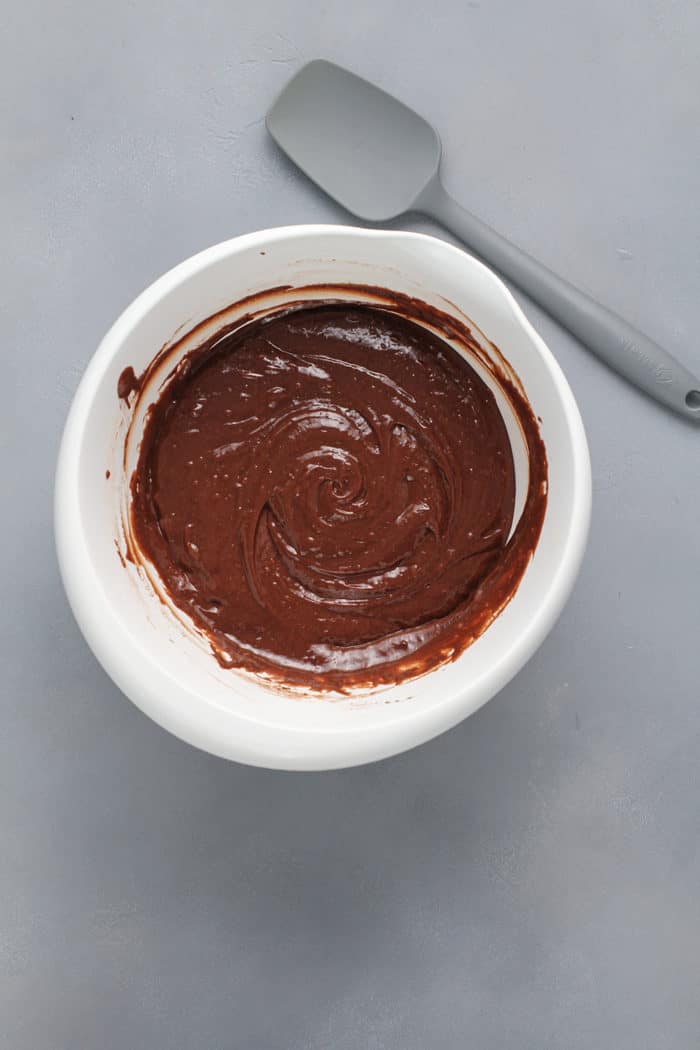 Batter for easy chocolate bundt cake in a white mixing bowl next to a gray spatula