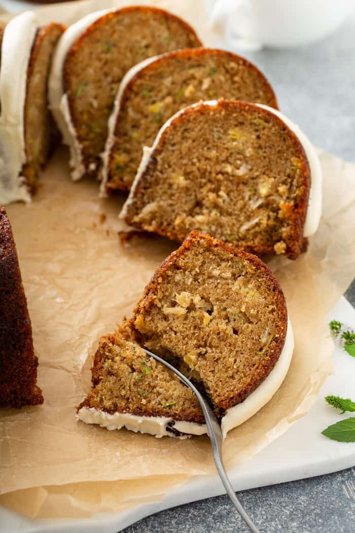 Fork cutting into a slice of zucchini bundt cake set on a piece of parchment paper, with more slices of cake in the background