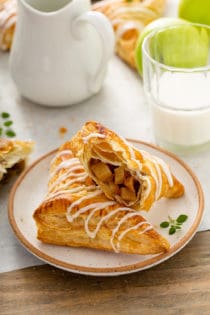 Two apple turnovers arranged on a plate, with one of the turnovers cut in half to show the filling inside