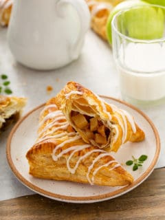Two apple turnovers arranged on a plate, with one of the turnovers cut in half to show the filling inside