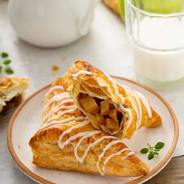 Two apple turnovers arranged on a plate, with one of the turnovers cut in half to show the filling inside