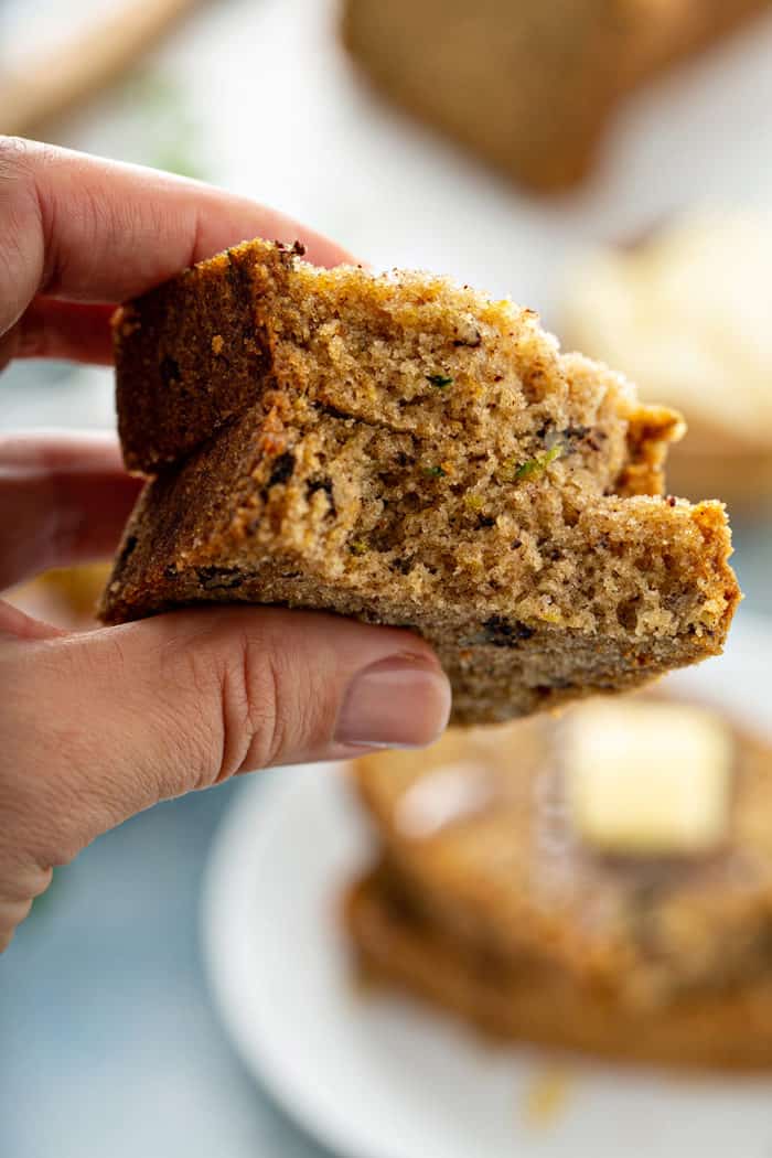 Hand holding up a piece of zucchini bread to the camera to show the texture