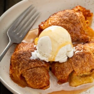 Easy apple dumplings topped with a scoop of ice cream and caramel sauce nestled in a cream bowl