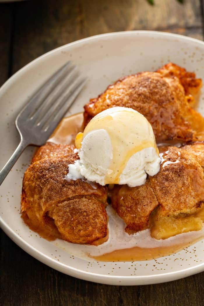 Easy apple dumplings topped with a scoop of ice cream and caramel sauce nestled in a cream bowl