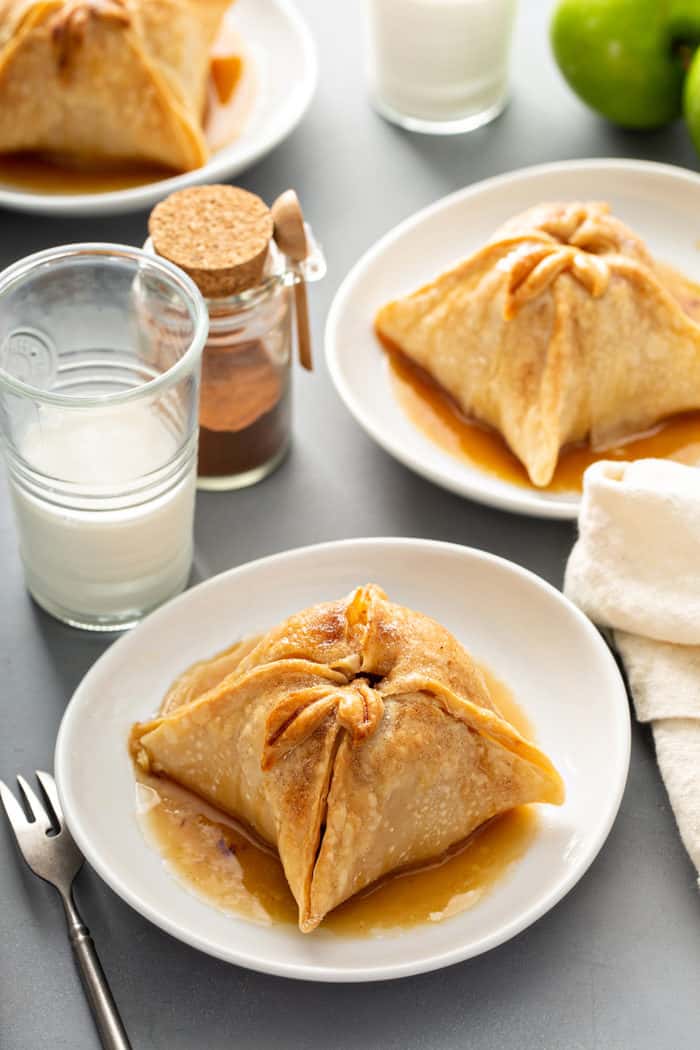 Three white plates containing old-fashioned apple dumplings set on a gray countertop