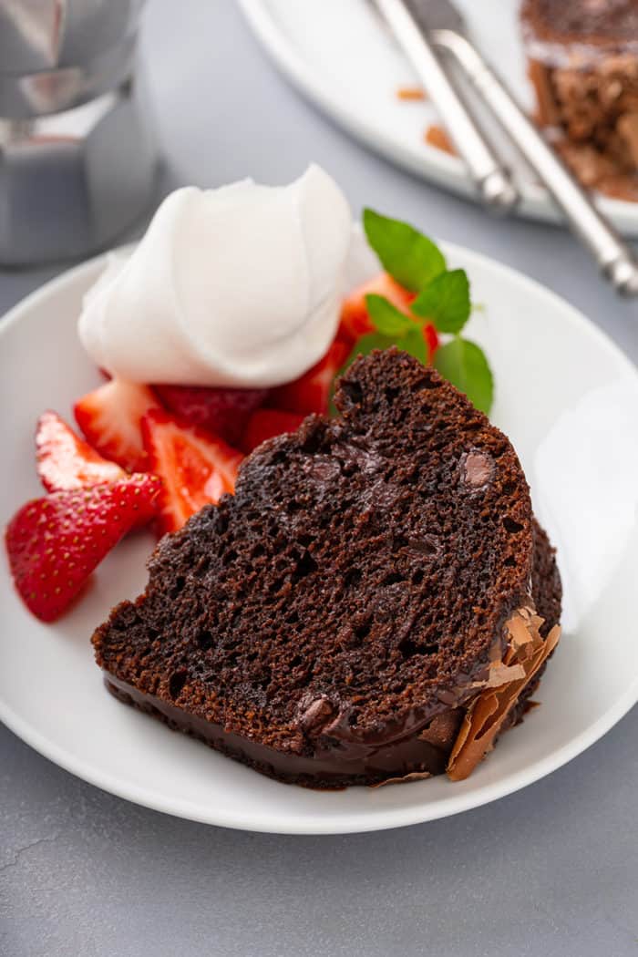 Slice of chocolate bundt cake next to berries and whipped cream on a white plate