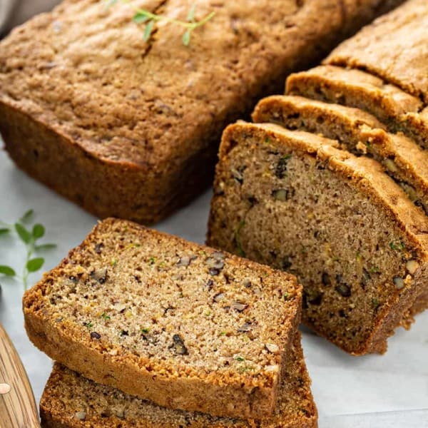 Two loaves of classic zucchini bread on a cutting board, with several slices cut from one of the loaves