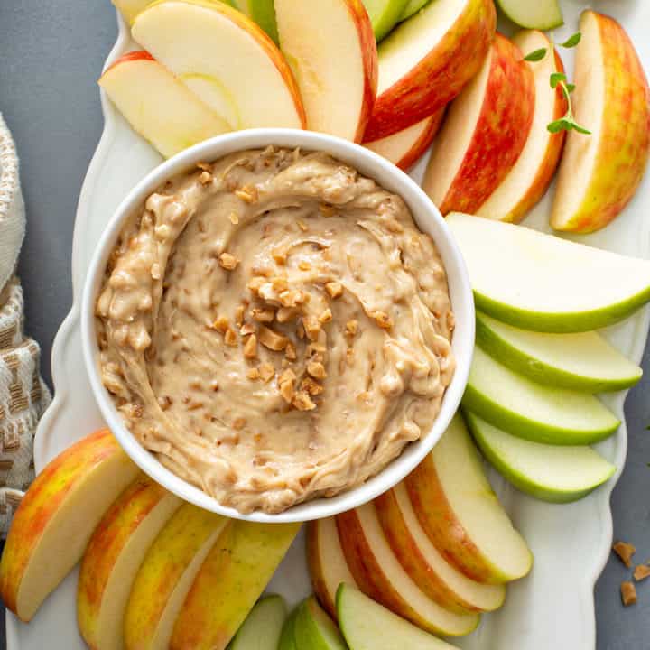 Overhead view of a bowl of toffee apple dip surrounded by fresh apples on a white platter