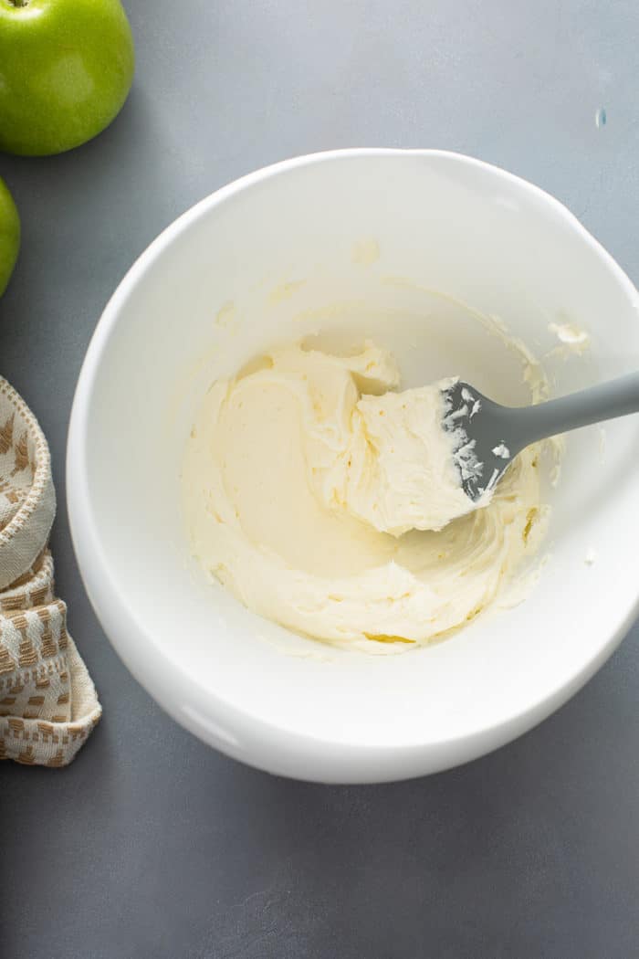 Spatula stirring whipped cream cheese in a white mixing bowl