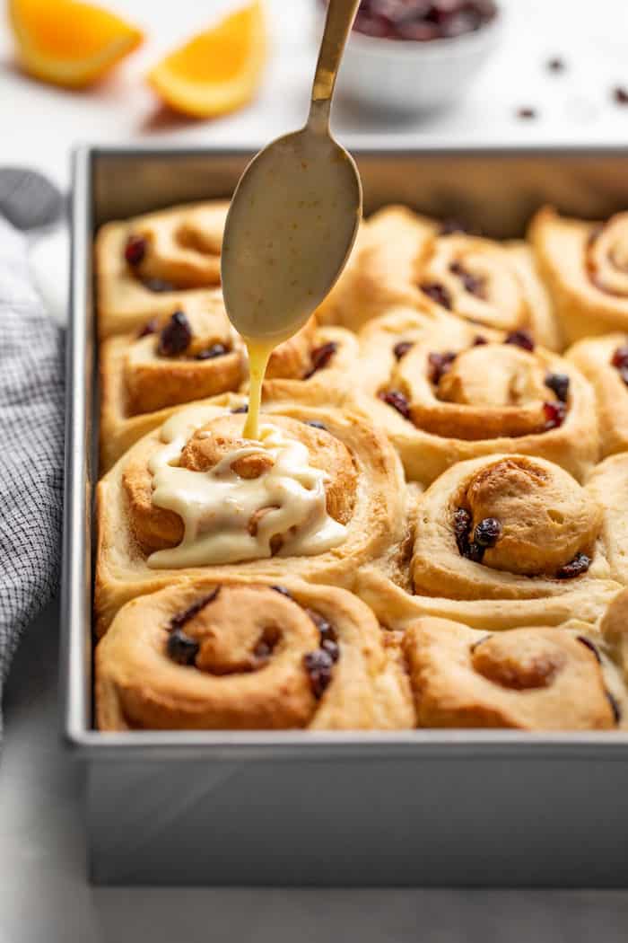 Spoon drizzling icing over the top of cranberry orange cinnamon rolls