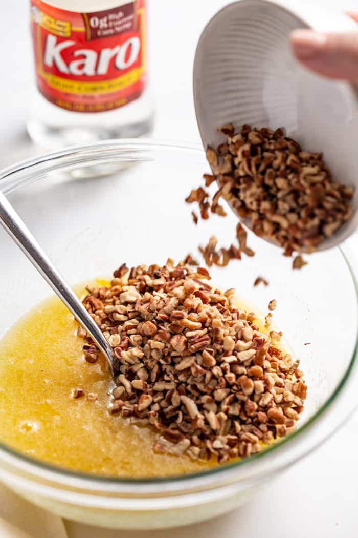 Pecans being added to pecan pie filling in a glass mixing bowl