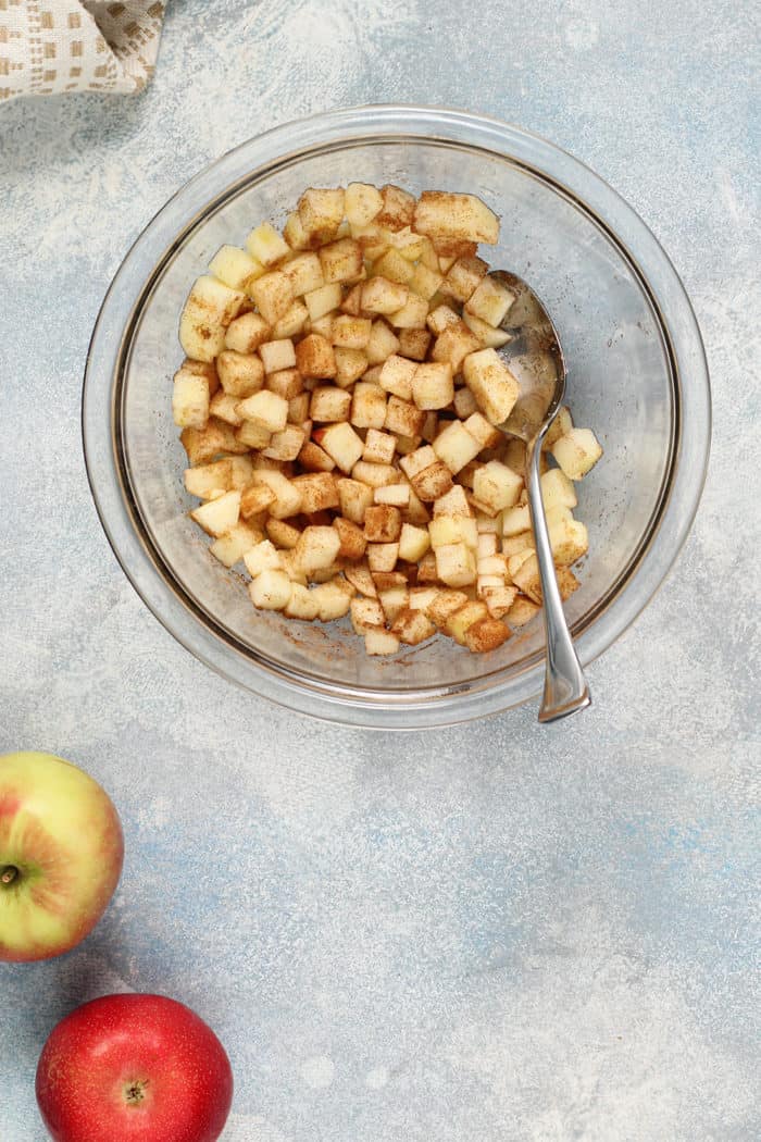 Spoon stirring diced apple filling for apple fritter bread in a glass bowl