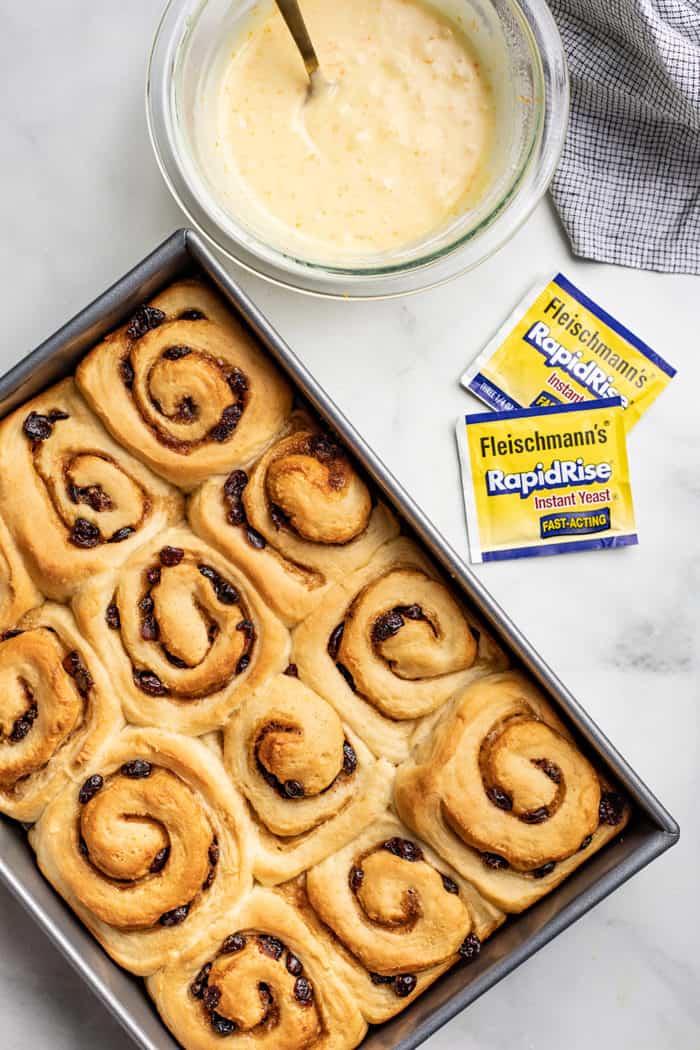 Baked cranberry orange cinnamon rolls on a marble countertop next to a bowl of icing