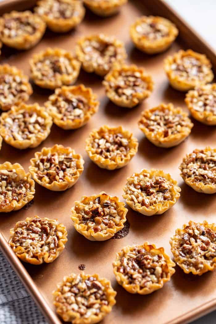 Baked mini pecan pies arranged on a baking sheet