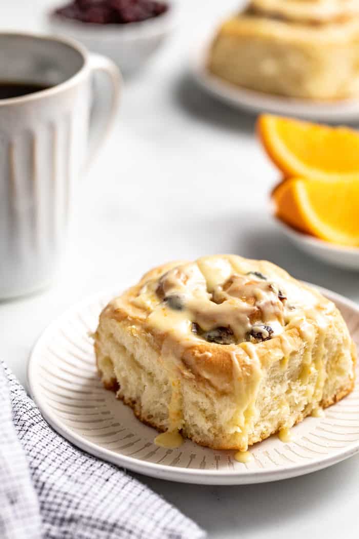 Cranberry orange cinnamon roll on a white plate with a cup of coffee in the background