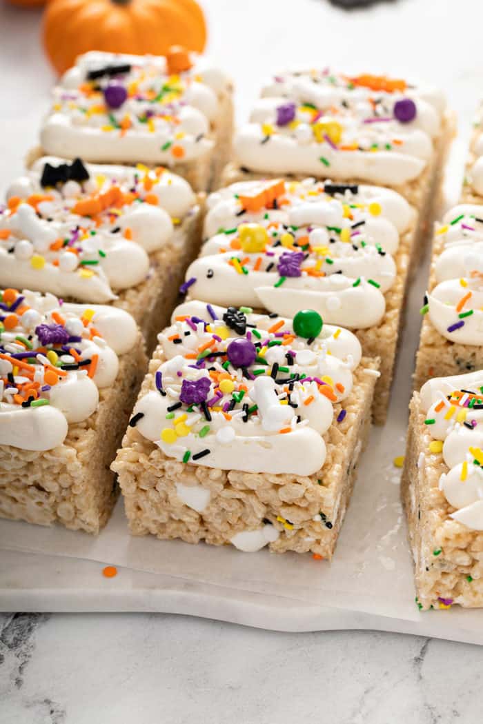 Frosted Halloween rice krispie treats topped with Halloween sprinkles on a piece of parchment paper