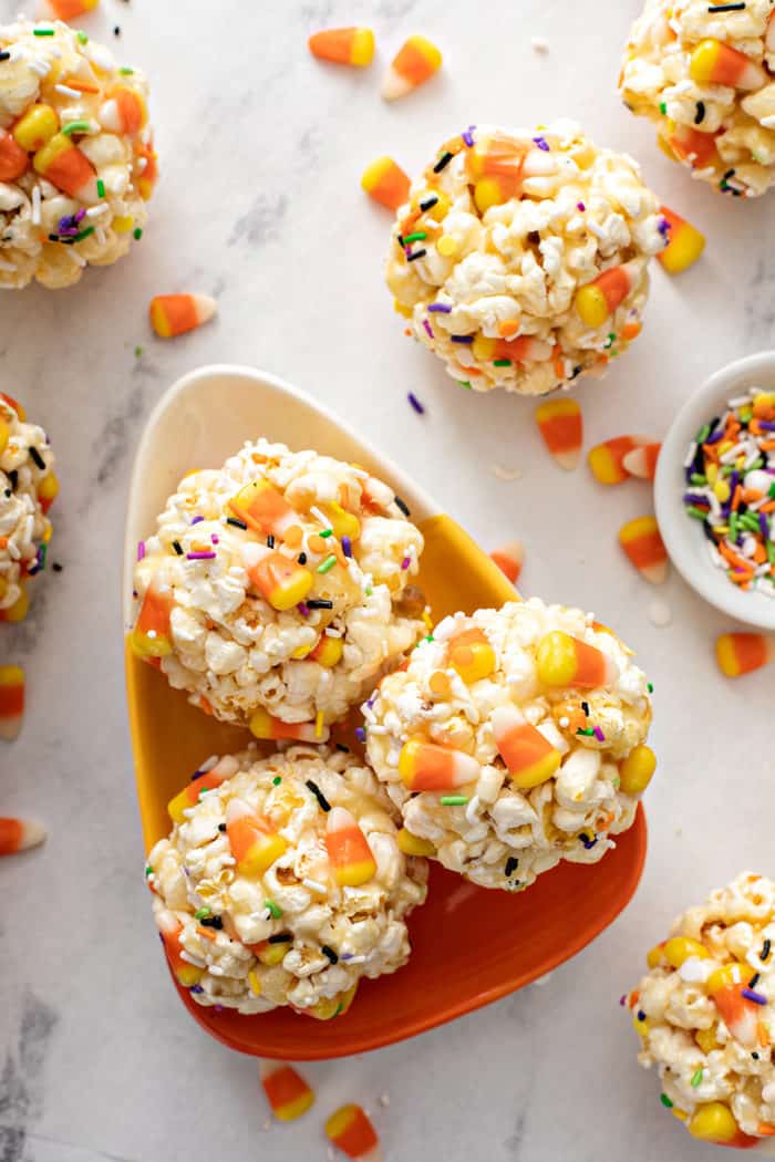 Candy-corn-shaped plate with three halloween popcorn balls set on a marble countertop
