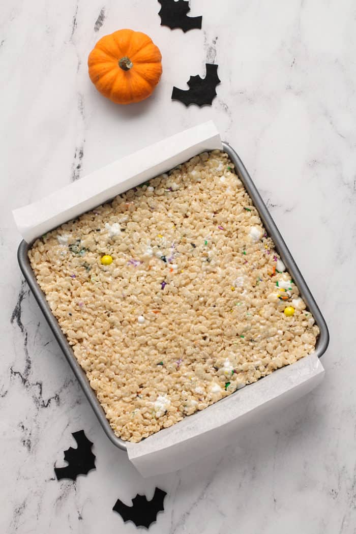 Unfrosted halloween rice krispie treats in a parchment-lined metal pan