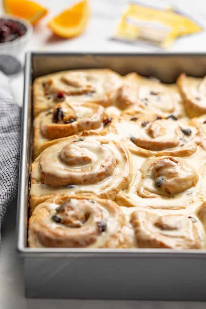 Cranberry orange cinnamon rolls with frosting in a metal baking pan