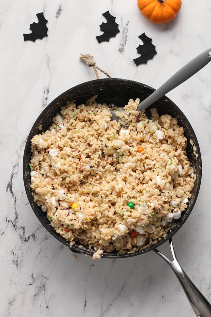 Halloween rice krispie treats being mixed with a spatula in a saucepan