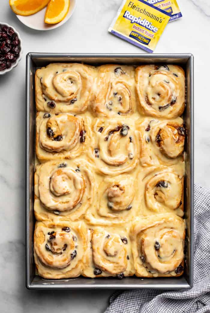 Overhead view of a pan of iced cranberry orange cinnamon rolls on a marble countertop