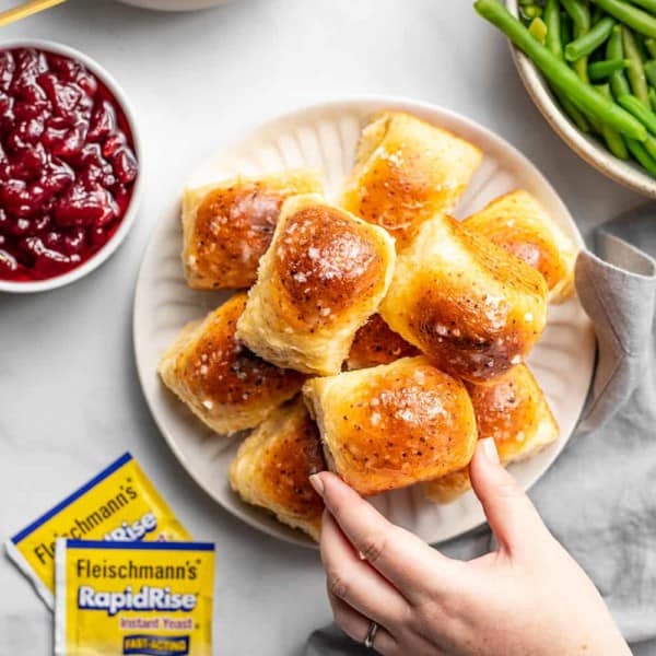 Hand grabbing a cheddar dinner roll off a plate of rolls