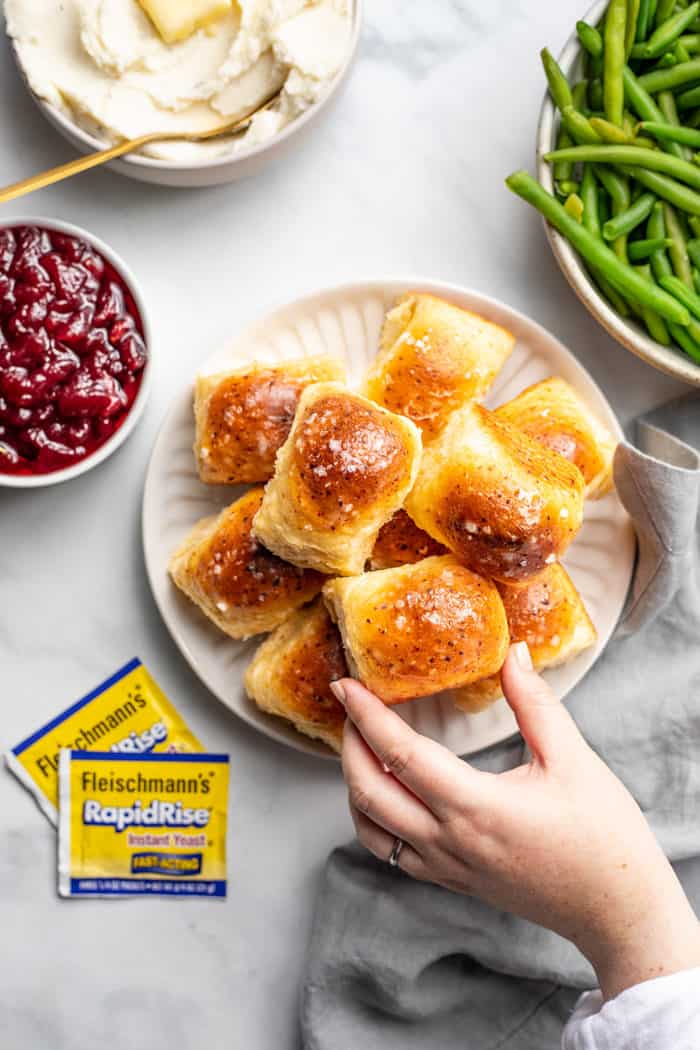 Hand grabbing a cheddar dinner roll off a plate of rolls