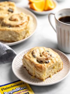 Plated cranberry orange cinnamon roll next to a cup of coffee