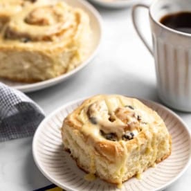 Plated cranberry orange cinnamon roll next to a cup of coffee