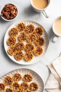 White plates filled with mini pecan pies on a white countertop next to cups of coffee