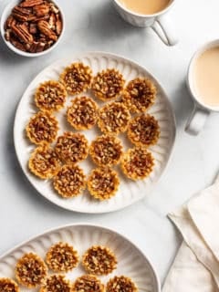 White plates filled with mini pecan pies on a white countertop next to cups of coffee