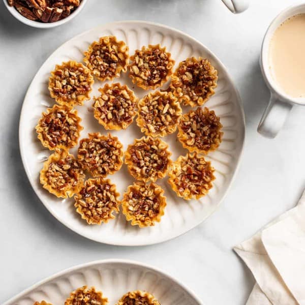 White plates filled with mini pecan pies on a white countertop next to cups of coffee