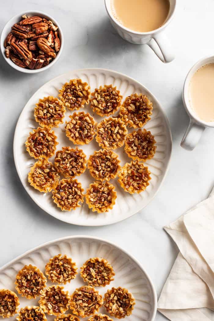 White plates filled with mini pecan pies on a white countertop next to cups of coffee