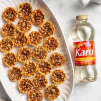 Overhead view of mini pecan pies on a white platter, set next to a bottle of corn syrup on a countertop
