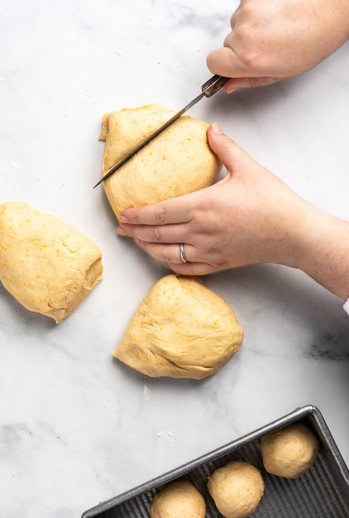 Hand portioning dough to shape cheddar dinner rolls