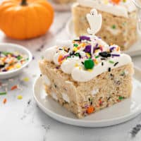 Halloween rice krispie treat, topped with seasonal sprinkles and a ghost cupcake topper, on a white plate