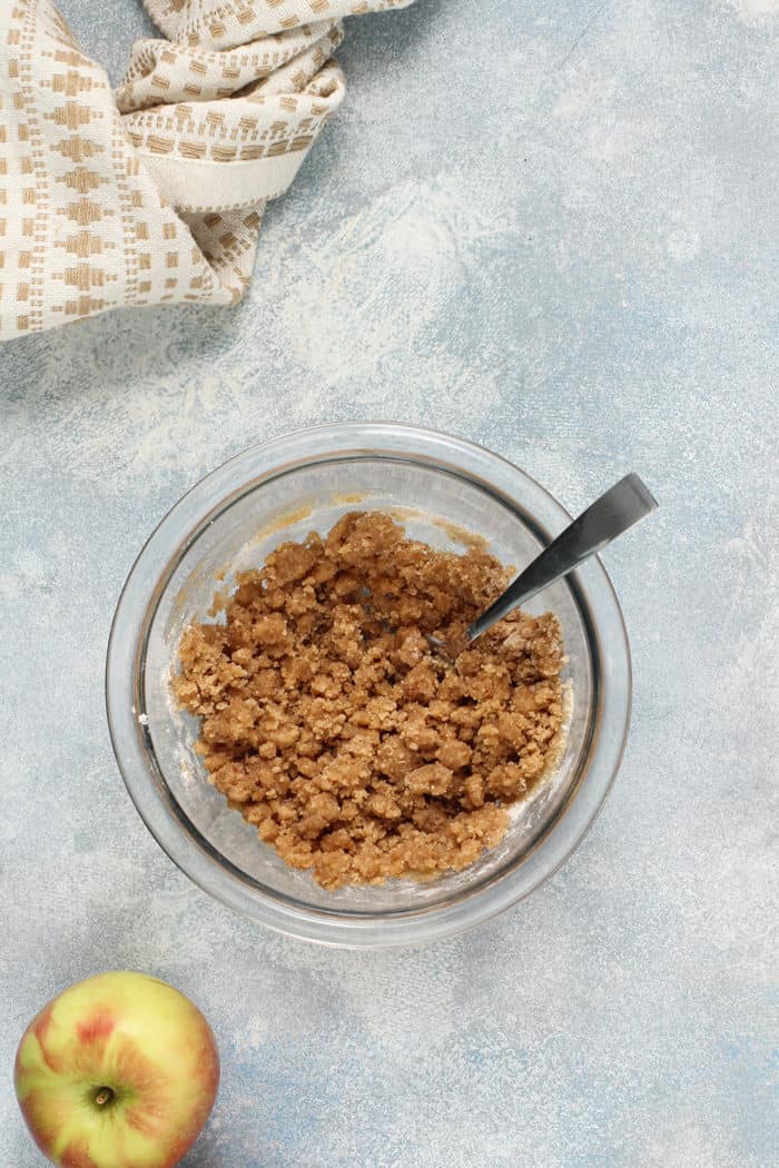 Spoon stirring streusel for apple fritter bread in a glass bowl