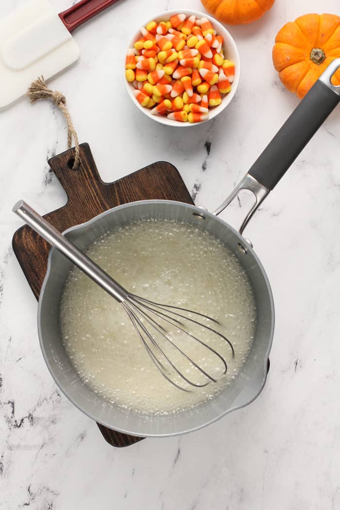 Whisk stirring together the syrup for halloween popcorn balls in a saucepan