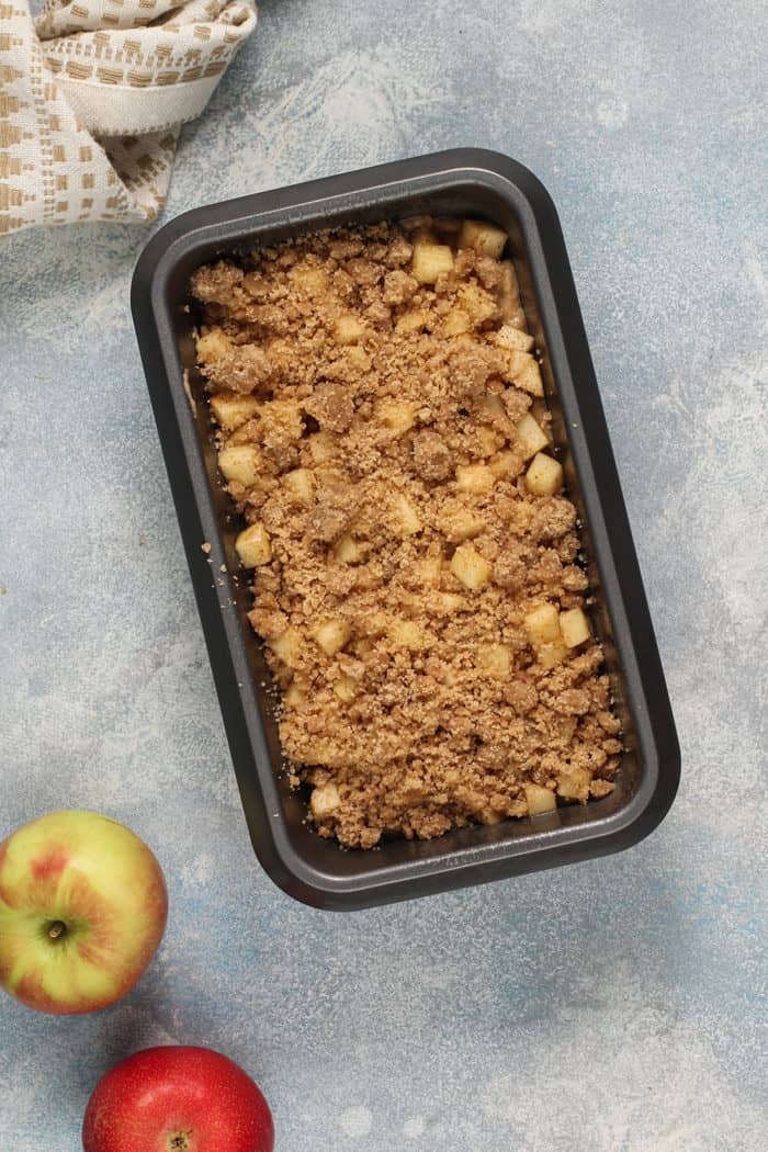 Unbaked apple fritter bread in a loaf pan, set on a blue countertop